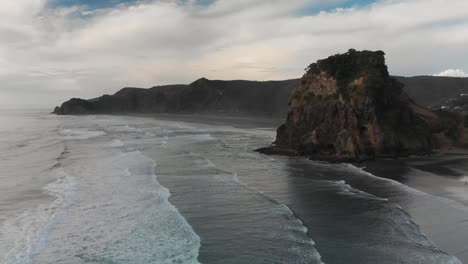 SLOWMO---Aerial-drone-shot-of-Piha-Beach-and-Lion-Rock-in-New-Zealand