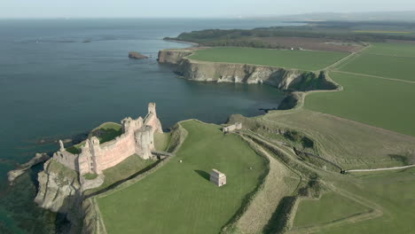 An-aerial-view-passing-over-Tantallon-Castle-ruin-with-the-castle-to-the-left-hand-side-of-frame-on-a-sunny-day,-East-Lothian,-Scotland
