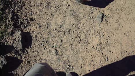 Camera-looks-straight-down-at-the-feet-of-a-male-in-hiking-boots-walking-across-sand-in-the-American-Southwest