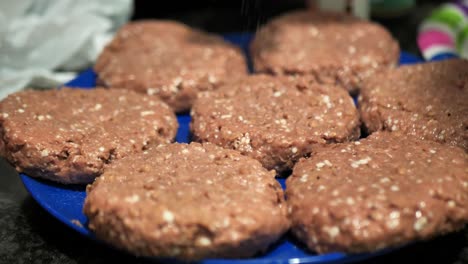 Seasoning-plant-based-burger-patties-on-a-blue-plate-for-a-summertime-barbecue-cookout,-in-60-frames-per-second-4k