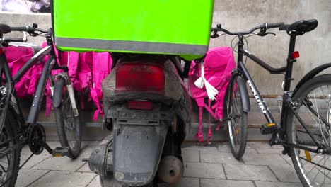 Bicicletas-De-Entrega-De-Alimentos-Y-Bolsas-Alineadas-Contra-La-Pared-En-Un-Entorno-Urbano-A-Cámara-Lenta