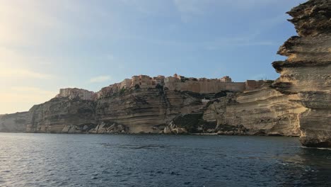 Moving-foward-toward-Bonifacio-Corse-city-perched-on-high-cliff-seen-from-navigating-sailboat-in-Mediterran-sea,-Corsica-in-France