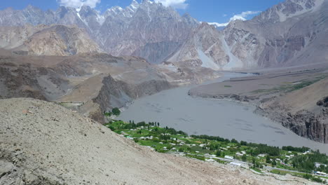 Wide-aerial-shot-of-Passu-Cones-and-village-or-town-in-Pakistan-with-the-glacier-path,-titling-upward-drone-shot