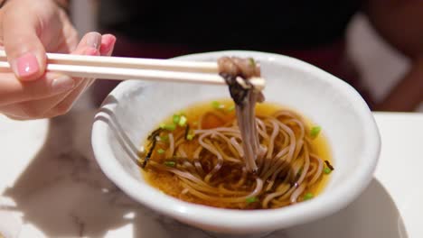 Woman's-hands-picking-up-Toshikoshi-Soba-Japanese-buckwheat-noodle-with-wooden-chopsticks-in-slow-motion-and-eat