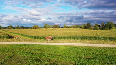 Tractor-trailer-in-front-of-golden-corn-field,-aerial-dolly-in-towards-storm-clouds