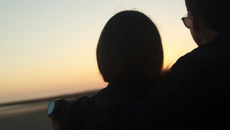 Couple-watching-the-sunset-and-hugging-at-the-beach,-handheld-close-up