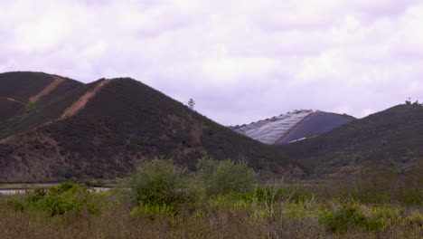 Three-mountains-in-the-footage-one-of-which-is-completely-stripped-of-all-plants-and-fully-occupied-by-solar-panels---wide-shot