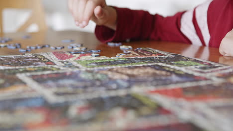 Side-view-of-a-seven-years-old-boy's-hands-assemble-puzzle-together-having-fun,-enjoy-game-at-home-sitting-on-the-table-in-the-livingr-room,-close-up