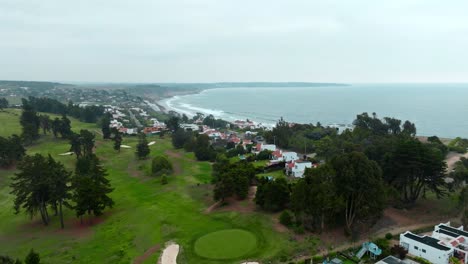 Dolly-in-aerial-view-of-exclusive-houses-with-their-own-golf-course-and-tiled-roof-in-a-small-town-with-ocean-view