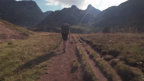 Back-view-of-hiker-with-big-backpack-walking-towards-mountain-peak-in-sunny-aftenoon-sunset-in-summer-1