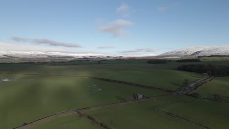 Aerial-pan-across-green-Lancaster-farmland-pastures-with-snowy-hills