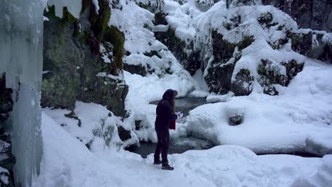 Woman-playing-in-the-snow-along-a-trail-at-a-stream-in-Alaska-while-it's-snowing