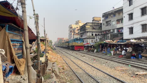 Local-passenger-train-passing-through-city-market-in-Dhaka,-Bangladesh---Handheld-Shot