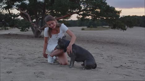 Weite-Sicht-Auf-Junge-Frau,-Die-Ihren-Amerikanischen-Staffordshire-Terrier-Hund-In-Sanddünen-Streichelt-Und-In-Richtung-Kamera-Blickt