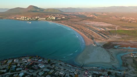 Vista-Aérea-Panorámica-De-La-Playa-De-Socos-En-El-Norte-De-Chile,-Con-Edificios-Y-Casas-Solitarias-En-Las-Montañas-A-Los-Lados,-Día-Soleado