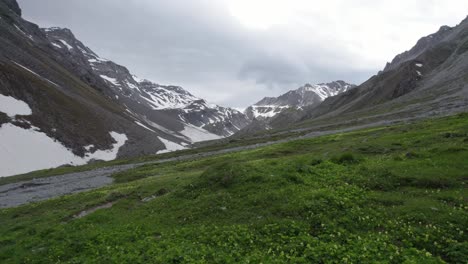 Aerial-drone-footage-flying-along-a-hiking-trail-in-a-glacial-mountain-landscape-with-patches-of-snow-and-a-remote-alpine-meadows-full-of-wild-flowers-in-Switzerland