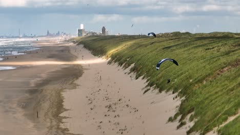 Aerial-tracking-shot-of-paraglider-flying-over-sandy-beach-and-dunes-of-Netherlands