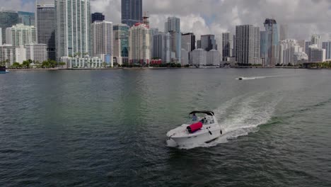 Aerial-view-around-guys-in-a-boat,-driving-off-the-coast-of-Miami-Skyline-2