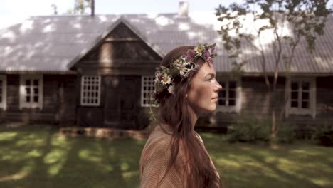 A-woman-with-the-flower-crown-is-walking-by-an-ancient-cottage-as-the-camera-is-following-her,-colour-graded,-slow-motion