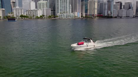 Aerial-view-around-guys-in-a-boat,-driving-off-the-coast-of-Miami-Skyline-1