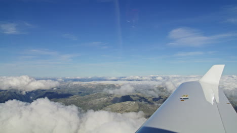 Blick-Aus-Einem-Flugzeugfenster-Hinunter-Auf-Wolken-Und-Bergketten