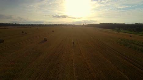 A-lone-man-with-a-backpack-walking-across-a-harvested-field-with-straw-bales-to-a-romantic-sunset-in-the-distance