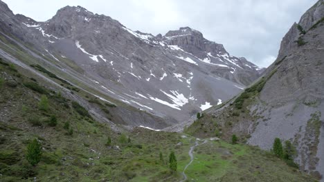 Drohnenaufnahmen-Aus-Der-Luft,-Die-Sich-Gerade-Nach-Oben-Erheben,-Um-Eine-Gletscherberglandschaft-Mit-Schneeflecken,-Vereinzelten-Bäumen-Und-Einem-Abgelegenen-Alpinen-Wanderweg-In-Der-Schweiz-Zu-Enthüllen