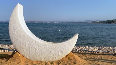 Half-moon-lamp-on-sandy-beach-in-front-of-sea-for-preparation-of-venue-decoration-for-celebration-event
