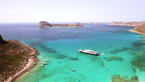 Static-Aerial-Shot-of-Day-Cruise-Boat-Manoeuvring-at-Balos-Beach-in-Crete,-Greece-in-Beautiful-Turquoise-Water-on-Sunny-Day