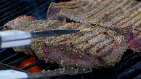 A-pair-of-meat-tongs-nudge-a-nearly-cooked-juicy-rib-eye-steak-on-a-grill-and-slides-it-a-bit-in-slow-motion