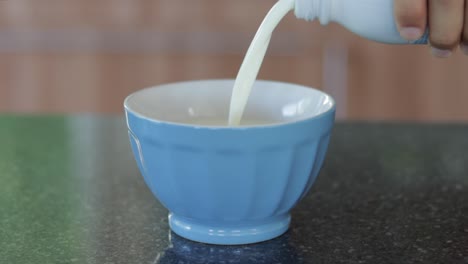 pouring-milk-from-bottle-into-blue-bowl-in-home-kitchen-on-modern-counter,-close-up-still
