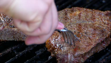 A-fork-and-knife-cutting-a-rib-eye-steak-on-the-grill-to-see-how-pink-the-meat-is-on-the-inside-whether-it’s-rare,-medium-or-well-done-in-slow-motion