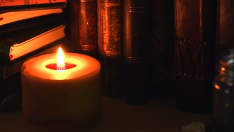 Nahaufnahme-Hintergrund-Einer-Alten-Bibliothek,-Neben-Einem-Friplace,-Mit-Alten-Büchern,-Tinte-Und-Einer-Kerze-Mit-Flackernder-Flamme