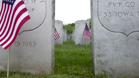 Close-up-view-of-old-white-gravestones-of-veterans-in-a-cemetery-on-memorial-day-in-a-graveyard-with-American-flags