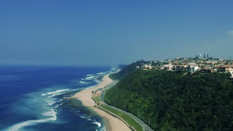 Aerial-footage-filmed-of-the-Bluff-Beach-overlooking-residential-houses-on-a-hillside-then-tilting-down-towards-the-beach-with-sea-views-in-Durban-South-Africa