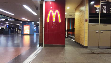 Editorial,-Timelapse-view-of-McDonald's-Logo-on-wall-beside-the-entrance-hall,-doorway-of-the-fast-food-restaurant,-showing-people-and-clients-passing-in-timelapse-motion