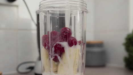 Pouring-milk-into-raspberries-and-banana-mix-to-make-vitamin-smoothie