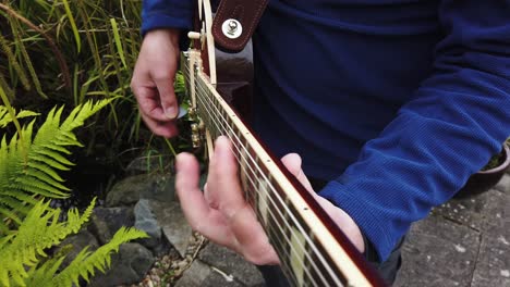 Practicing-playing-rock-music-on-electric-guitar-in-the-garden-near-the-pond
