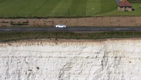 Aerial-profile-shot,-tracking-traffic-along-the-chalk-clifftop-coast-road,-A259-near-Brighton,-UK