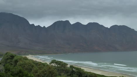 Waves-running-onto-long-stretch-of-pristine-beach-in-beautiful-setting,-next-to-mountain,-shot-from-high-vantage-point,-South-Africa