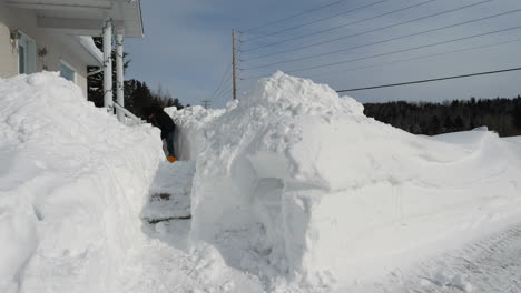 Man-shoveling-a-lot-of-snow-off-walkway-in-front-of-snowbound-house