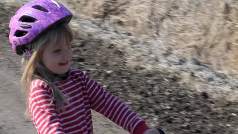 Young-little-girl-rides-a-running-bike-on-a-gravel-road-in-rural-landscape,-good-way-to-gain-balance-for-kids-learning