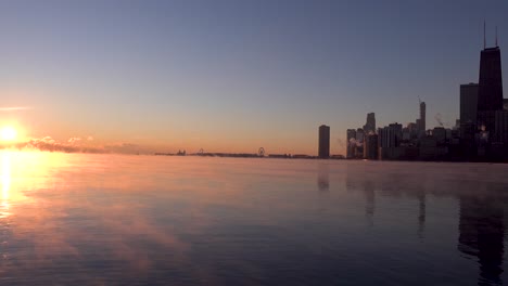 Sun-rising-over-Lake-Michigan-horizon-over-Chicago-downtown-skyline-in-winter-with-sea-smoke-in-water-during-polar-vortex-4k