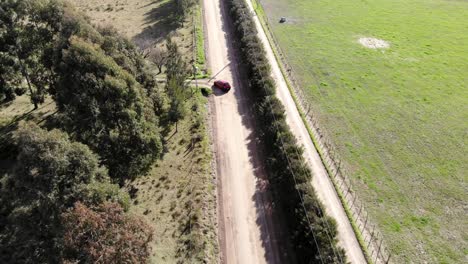 Aerial-shot-of-car-driving-on-road-in-a-countryside-with-dirt-street