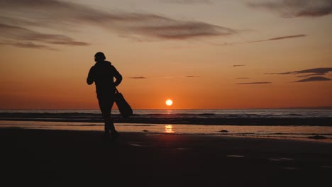 Mann-Läuft-Mit-Gitarre-Im-Hinteren-Sandstrand-Bei-Sonnenuntergang