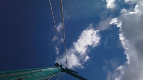 A-shot-from-below-of-a-mast,-with-a-background-of-blue-sky-and-cotton-clouds