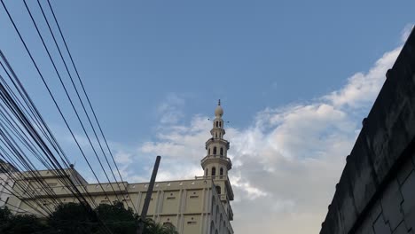 Torre-Del-Minarete-De-La-Mezquita-Símbolos-Del-Islam-Durante-El-Tiempo-De-Azan,-Incline-Hacia-La-Carretera-Llena-De-Tráfico,-Día