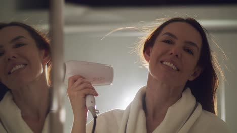 Brazilian-Brunet-using-a-Hairdryer-on-the-mirror-with-a-smile,-Slow-motion