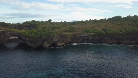 Sea-cliff-aerial-rises-to-reveal-distant-volcano-cone,-Bali-Indonesia
