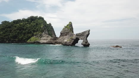 Jagged,-eroded-rock-of-Batupadasan-Island-stands-in-shallow-Bali-bay